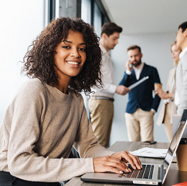 Mujer sonriendo con portatil y grupo de trabajores reunidos