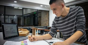 Estudiante con plano y computador en un salón