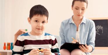 Niño jugando con ficha y mujer tomando nota del comportamiento