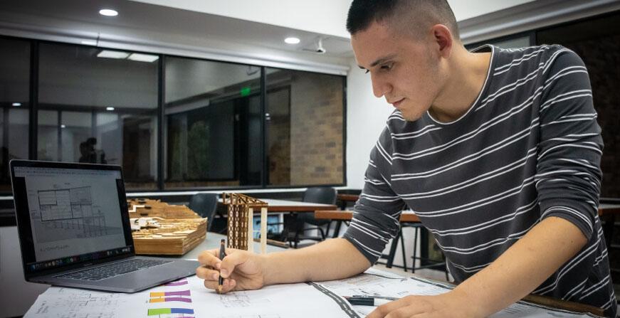 Estudiante con plano y computador en un salón