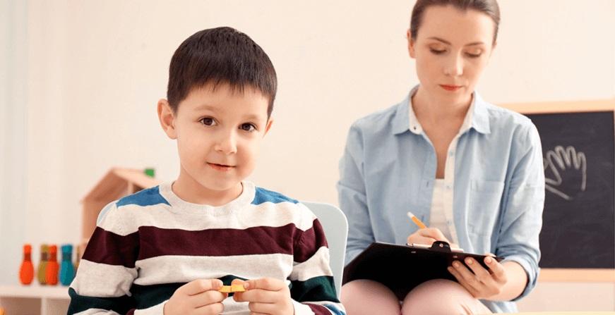 Niño jugando con ficha y mujer tomando nota del comportamiento